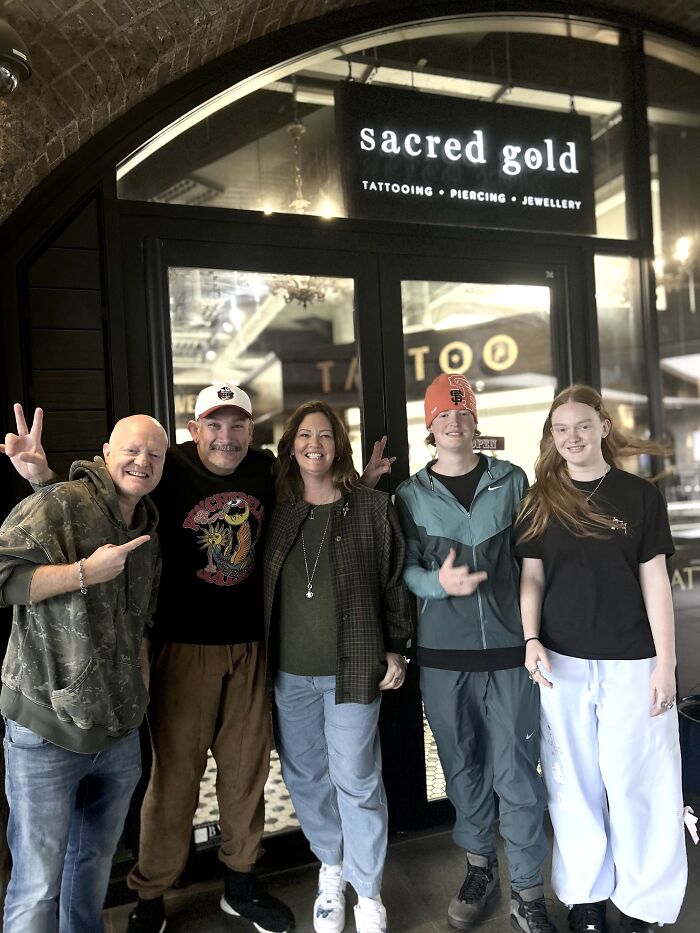 A group of five people smiling in front of a tattoo shop, showcasing their positive experience with matching ink ideas.