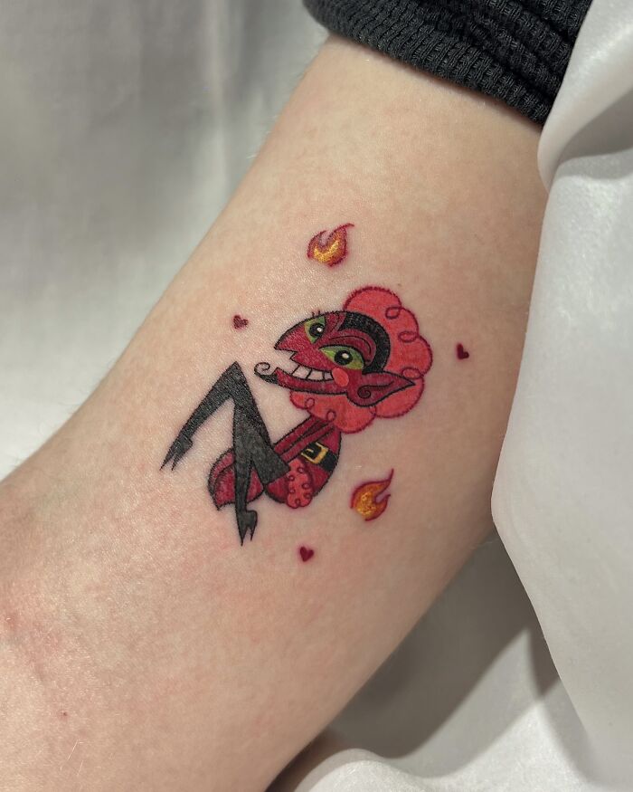 A vibrant tattoo inspired by crayon drawings, featuring a red devil character with green eyes and flames, showcasing creative childhood artistry.