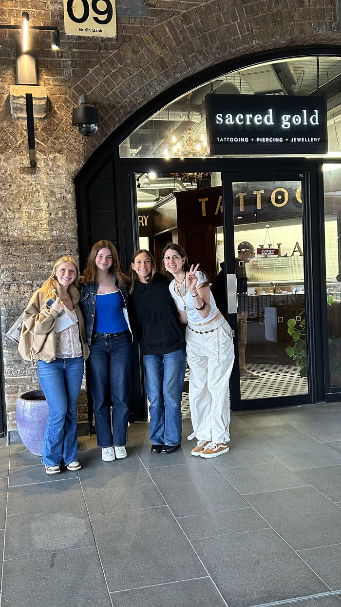 Four women stand outside Sacred Gold, a tattoo, piercing, and jewelry shop, showcasing matching ink ideas from tattoo artists.