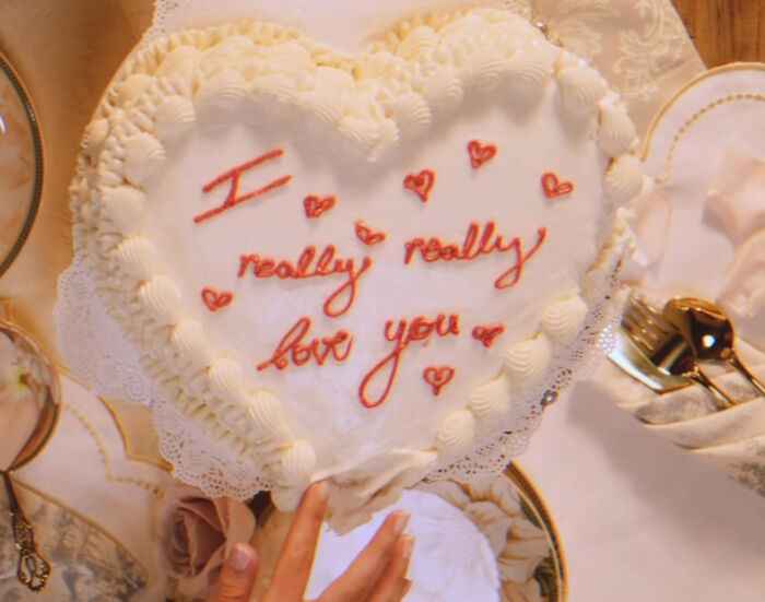 A heart-shaped cake with pink icing that reads 'I really really love you' on a table, part of a SYRN Lingerie theme.