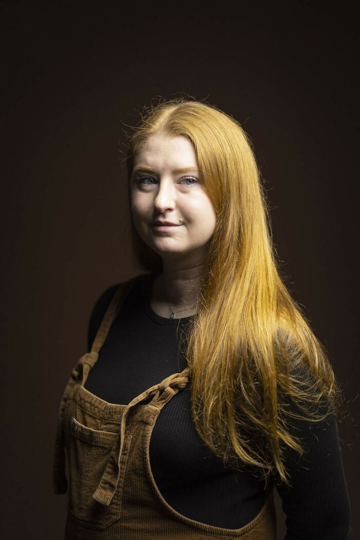 A young woman with long, flowing natural redheads hair and a serious expression, looking over her shoulder.