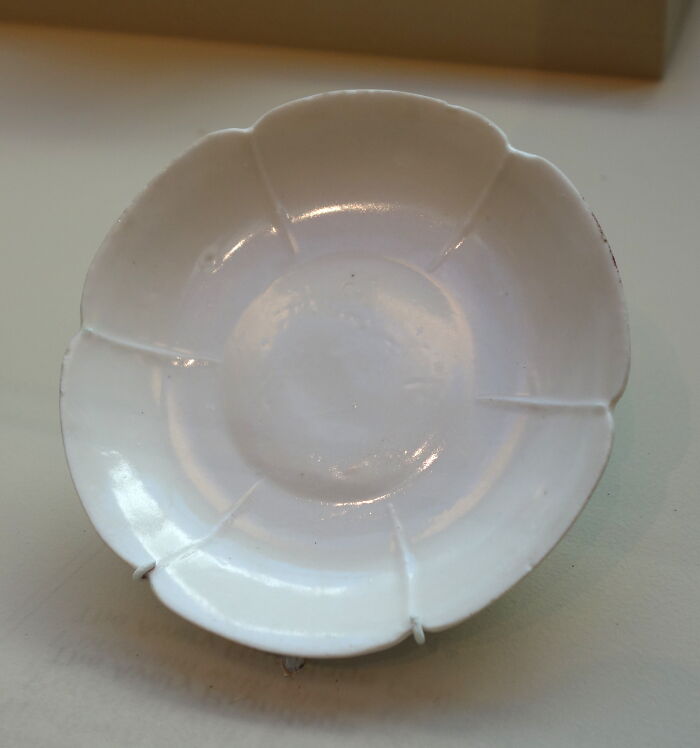 A small, white, decorative ceramic dish with a scalloped edge, a random thing people did that got them rich.