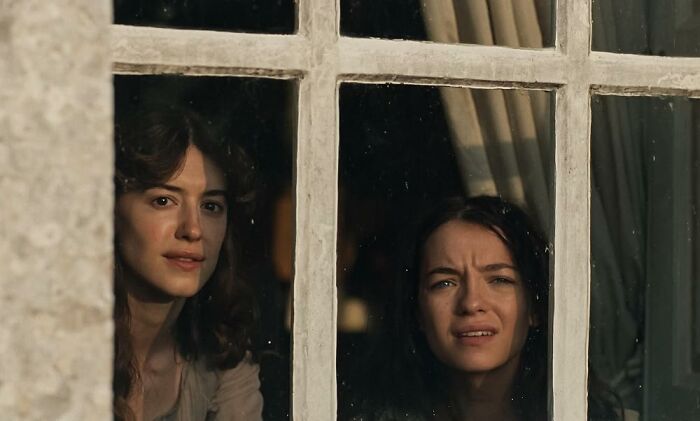 Two women looking out of a window with pained expressions, enjoying a Jane Austen adaptation. Two women looking out of a window with pained expressions, enjoying a Jane Austen adaptation.