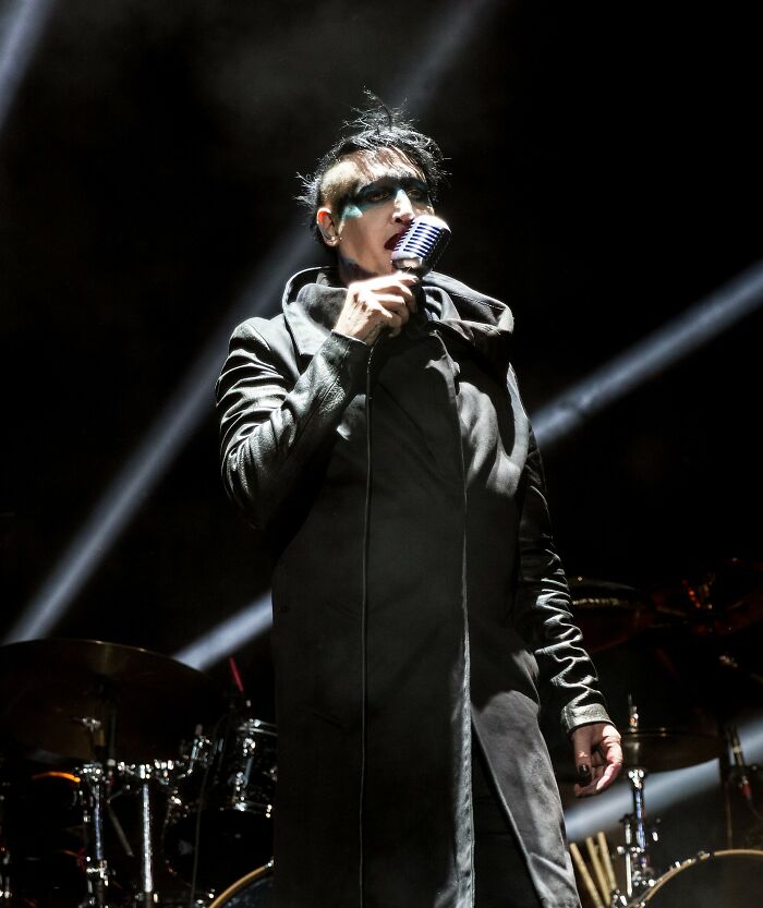 Marilyn Manson, a celebrity, performing on stage with a microphone in the spotlight.