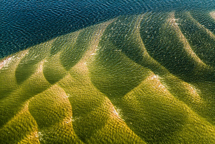 An aerial photo of stunning underwater sand dunes, reflecting light in a captivating way, a highlight from the Nature Photography Festival.