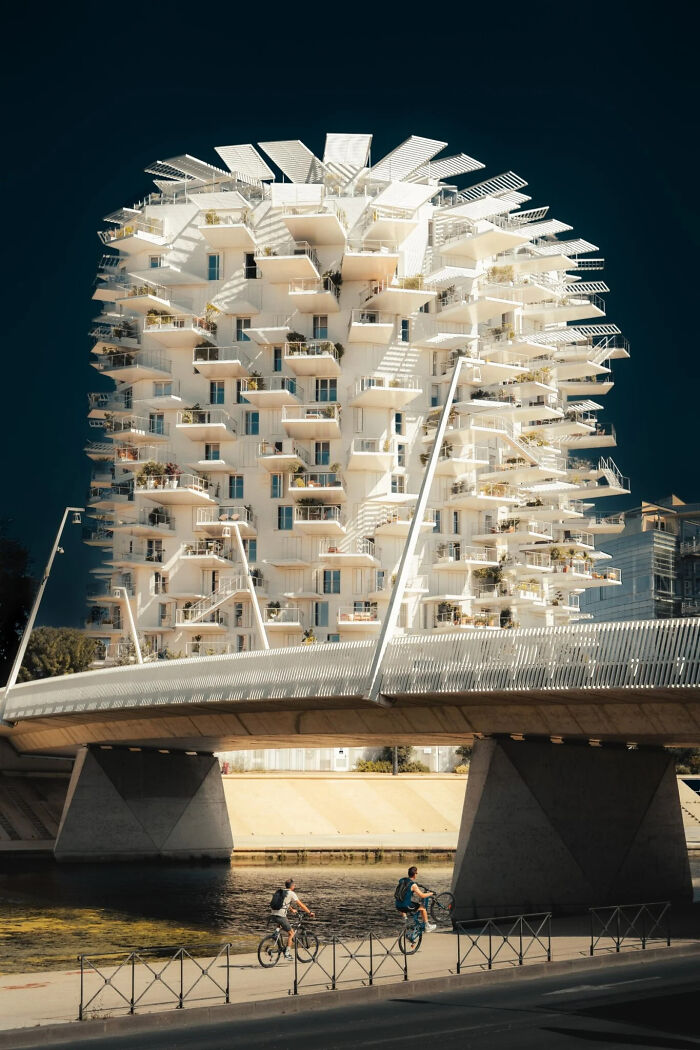 Modern, unique architecture of a multi-story white building with balconies, viewed from below a bridge, a winning image in the European Photography Awards.