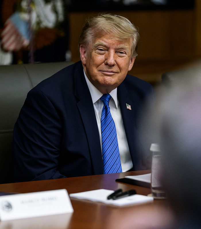 Trump smiling, seated at a table, not pictured with the mystery woman or her strange gesture. Trump smiling, seated at a table, not pictured with the mystery woman or her strange gesture.