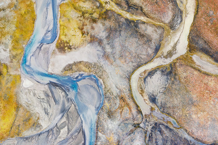 An abstract aerial view of winding rivers through colorful, textured terrain, featured in the Nature Photography Festival.