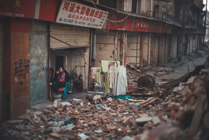 A woman sits amidst rubble, a poignant scene of the world, capturing a winning image for European Photography Awards.