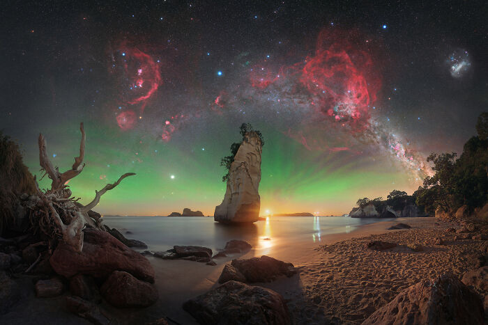 Stunning astronomy photo of a beach scene with a vibrant green aurora and red nebulae in the night sky.