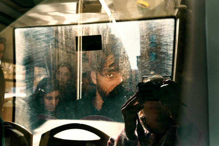 Reflected passengers and photographer in a bus window, a winning street photography image from the LensCulture Awards.