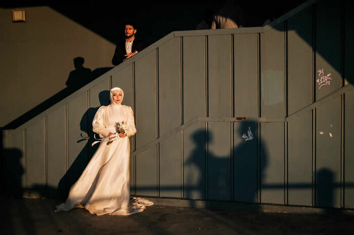 A woman in a white dress holds a bouquet on an outdoor staircase, a winning photo from LensCulture Street Photography Awards.