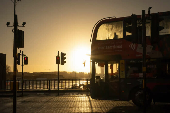 A double-decker bus is silhouetted against a brilliant sunset, a winning photo from LensCulture Street Photography Awards.