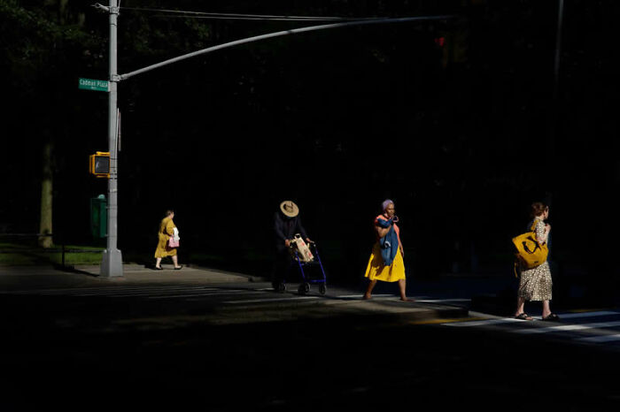 Pedestrians cross a dark street under a single streetlight, a winning photo from LensCulture Street Photography Awards.
