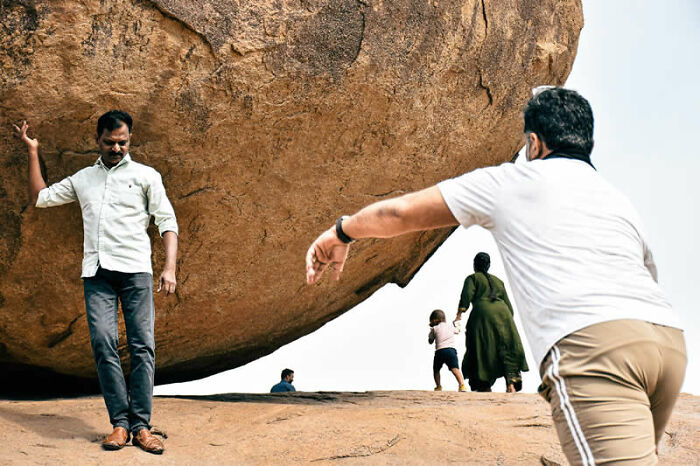 Two men appearing to move a giant boulder, with a family in the background, a captivating street photography awards image.