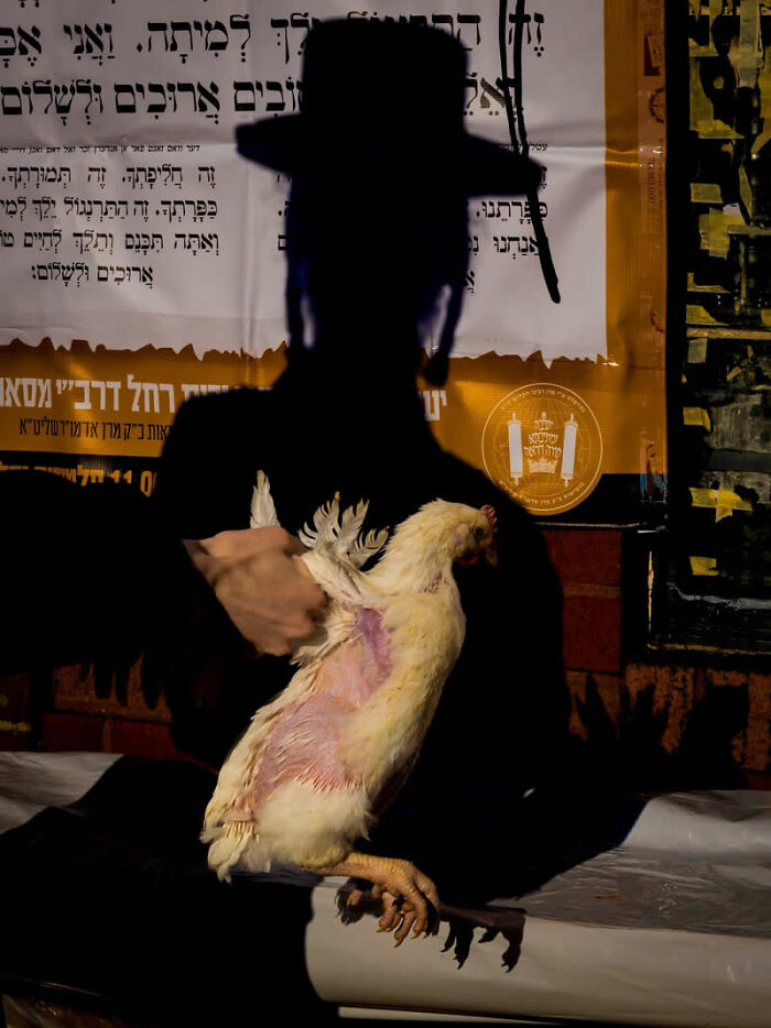 A silhouetted figure holding a chicken against a backdrop of Hebrew text, a powerful winning photo from the street photography awards.