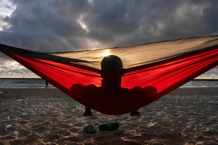 Person relaxing in a red hammock on a beach at sunset, a mesmerizing winning photo from the Street Photography Awards.