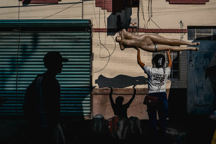 A person carries a mannequin through a sunlit street, showcasing a unique scene from the LensCulture Street Photography Awards.