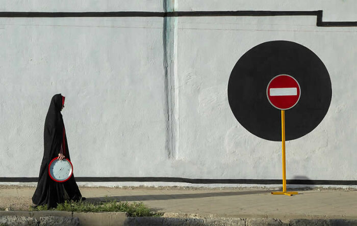 Woman in black walking past a large circular stop sign, a mesmerizing street photography award winner.