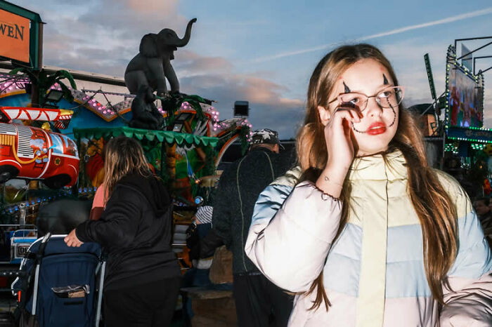A girl with clown makeup at an amusement park ride, a mesmerizing winning photo from the LensCulture Street Photography Awards.