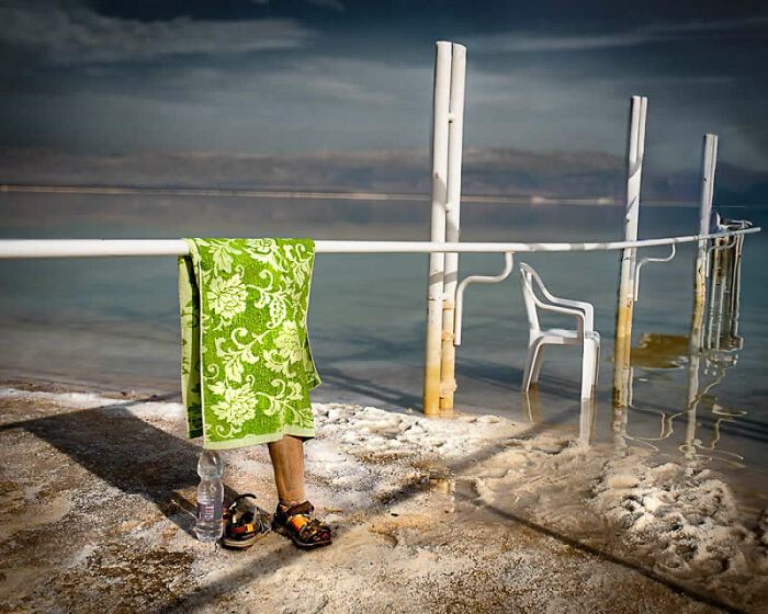 Legs of a person with a green towel and sandals on a salt-encrusted shore, a winning photo from the Street Photography Awards.