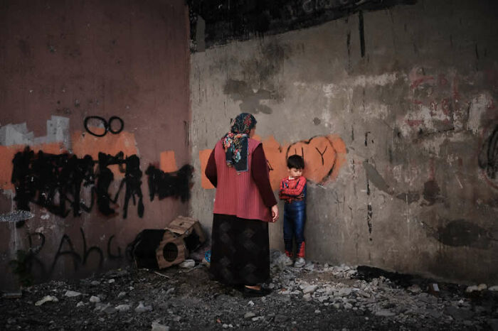 An adult and a child standing against a graffiti-covered wall in a desolate urban environment, a winning photo from the LensCulture Street Photography Awards.