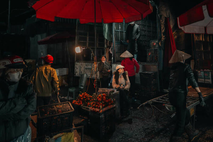 A bustling night market scene under red umbrellas, a mesmerizing winning photo from the LensCulture Street Photography Awards.