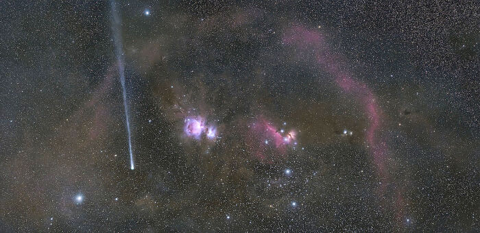 A long comet streaking across a dark sky with colorful nebulae and stars, a stunning David Malin Astrophotography Awards image.