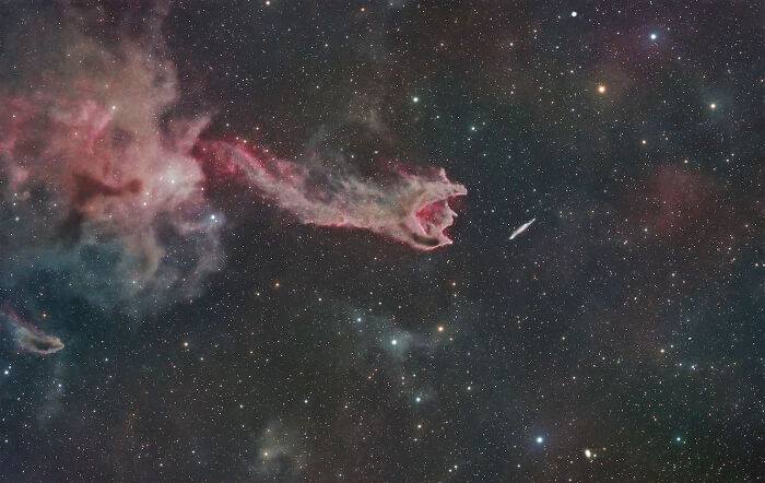 A vibrant cosmic cloud in red and teal, resembling a dragon, with a streak of light in deep space, a stunning astrophotography image.