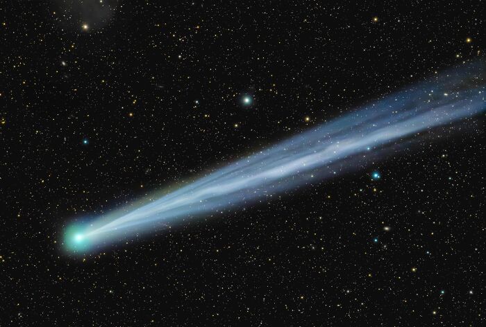 An award-winning astrophotography image capturing a comet with a brilliant blue tail, featured in the David Malin Astrophotography Awards.