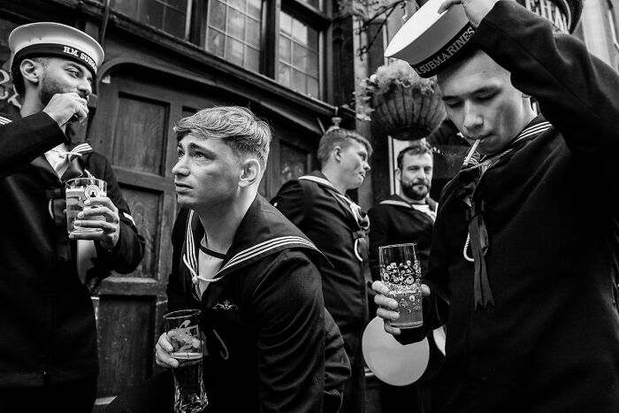 Black and white photo of sailors drinking outside a pub, capturing authentic street photography moments.