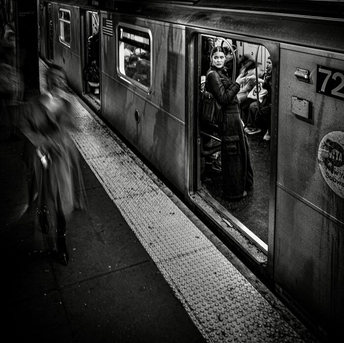 A person stands in a subway car door, watching a blurred figure on the platform in a striking street photography image.