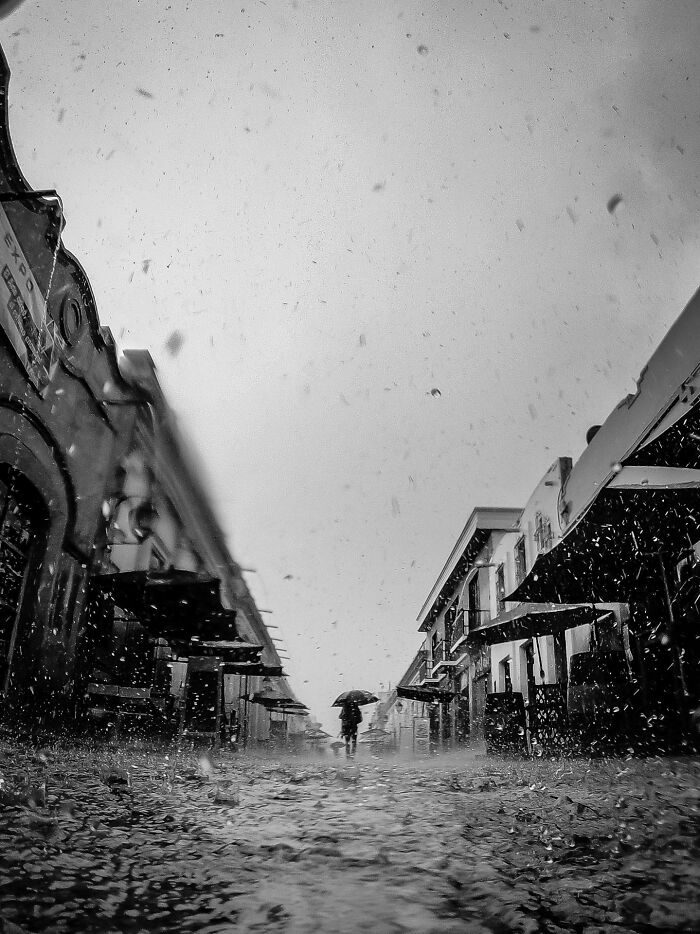 A lone figure with an umbrella walks down a street in the rain, capturing authentic moments of street photography.