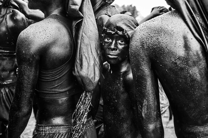 Boy with face painted black looking at camera amidst a crowd, an authentic street photography moment.