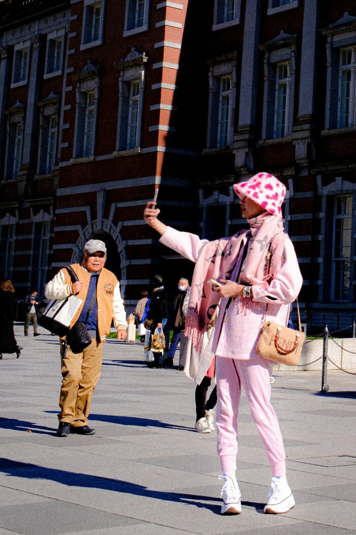 Woman in pink outfit taking a selfie, showing authentic street photography moments.