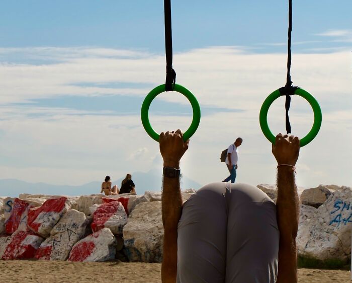 A person doing an inversion on gymnastic rings at a beach, showcasing authentic street photography.