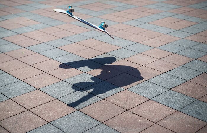 Skateboard in mid-air with its shadow on a checkered pavement, an dynamic street photography awards capture.