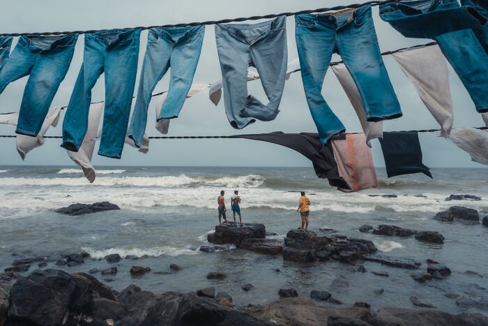 Ocean scene with drying jeans and three men on rocks, a pure street photography moment capturing life by the sea.
