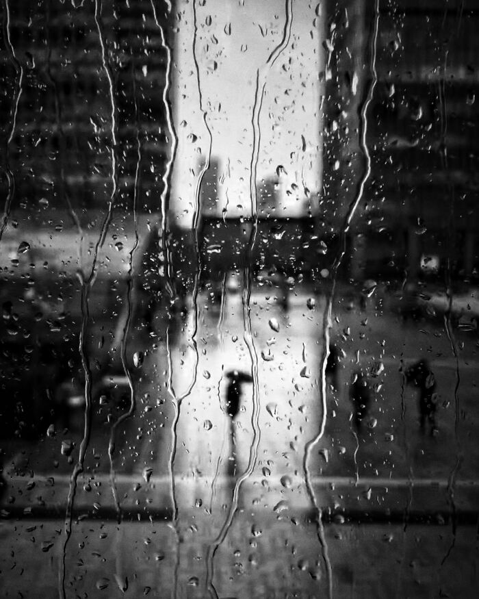 Pure street photography capturing a rainy window pane with blurred city reflections, creating authentic moments.