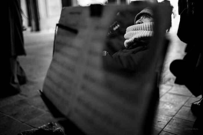 Pure street photography capturing a bundled-up person reflected in a music stand, showing authentic moments.