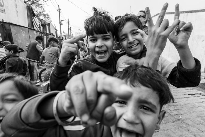 Pure street photography capturing three smiling children looking at the camera, one pointing, showcasing authentic moments.