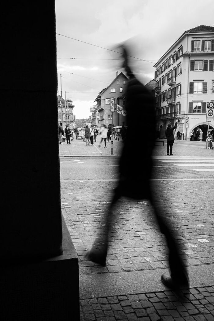 Blurred silhouette of a person walking across a cobblestone street.