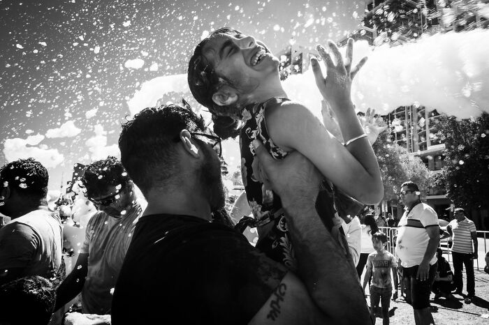 A man holding a laughing girl amidst foam and water, capturing authentic street photography moments.