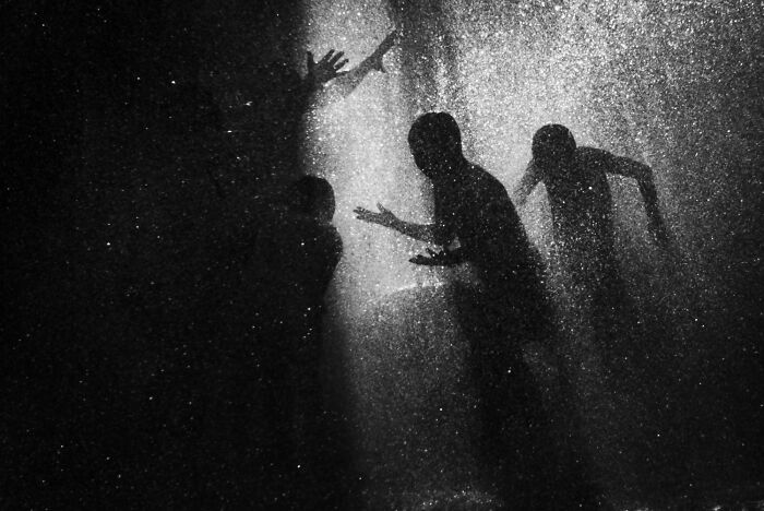Silhouettes of people playing in a fountain at night, showcasing authentic street photography.