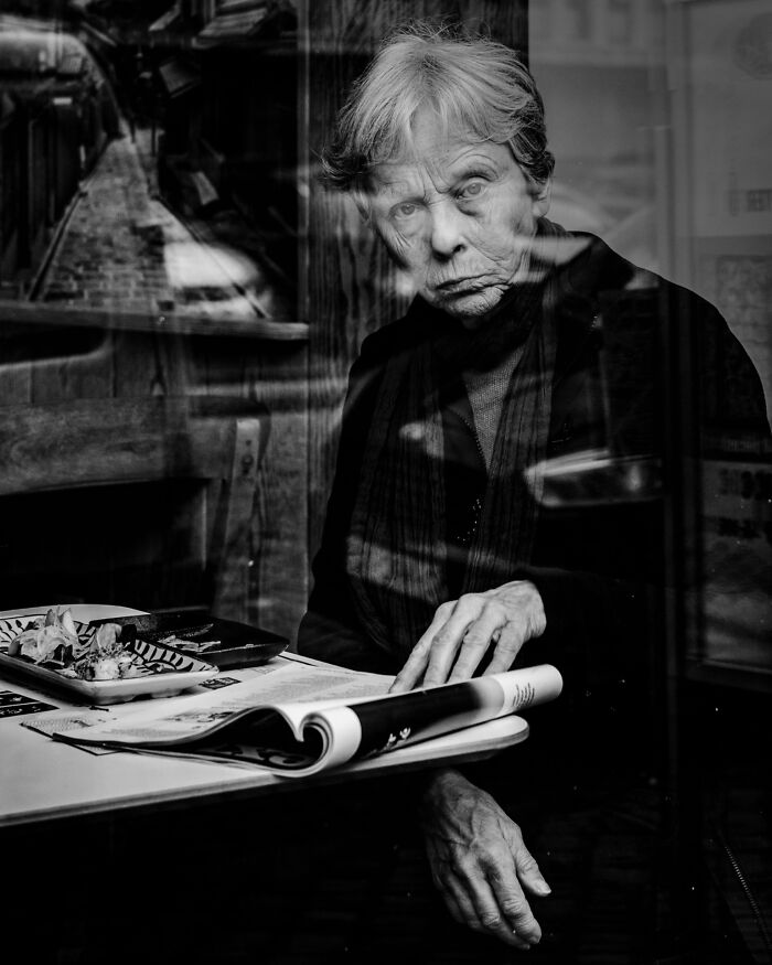 An elderly woman reading a magazine in a cafe, reflecting an authentic street photography scene.