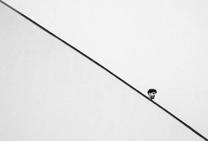 A man's head peeking over a diagonal line, minimalist street photography capturing an authentic moment.