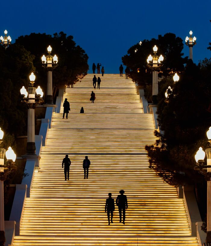 Murat Bakmaz captures the beauty of everyday life with people ascending an illuminated outdoor staircase at night.