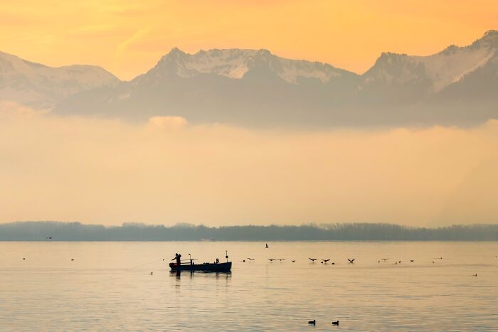Murat Bakmaz captures the beauty of everyday life with a boat on a misty lake against mountains at sunset.