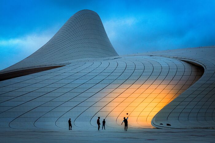 Murat Bakmaz captures the beauty of everyday life: Children playing with a ball in front of a modern, curvilinear building.