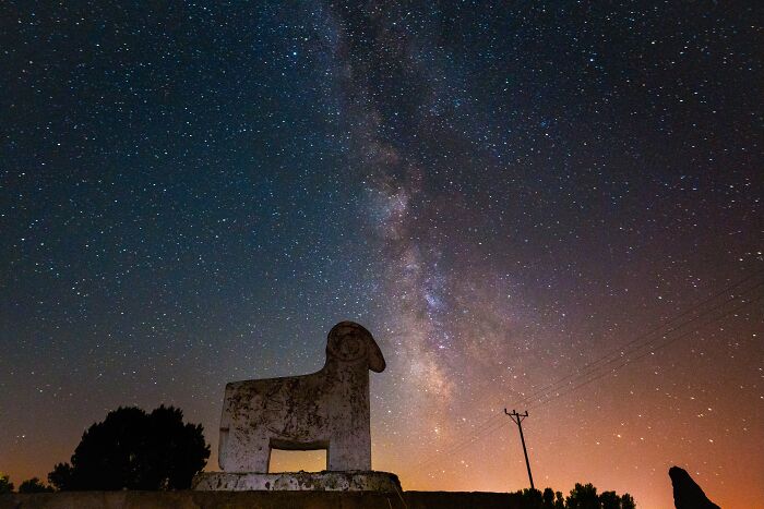 Murat Bakmaz captures the beauty of everyday life: A stone ram statue under a vibrant Milky Way at night.